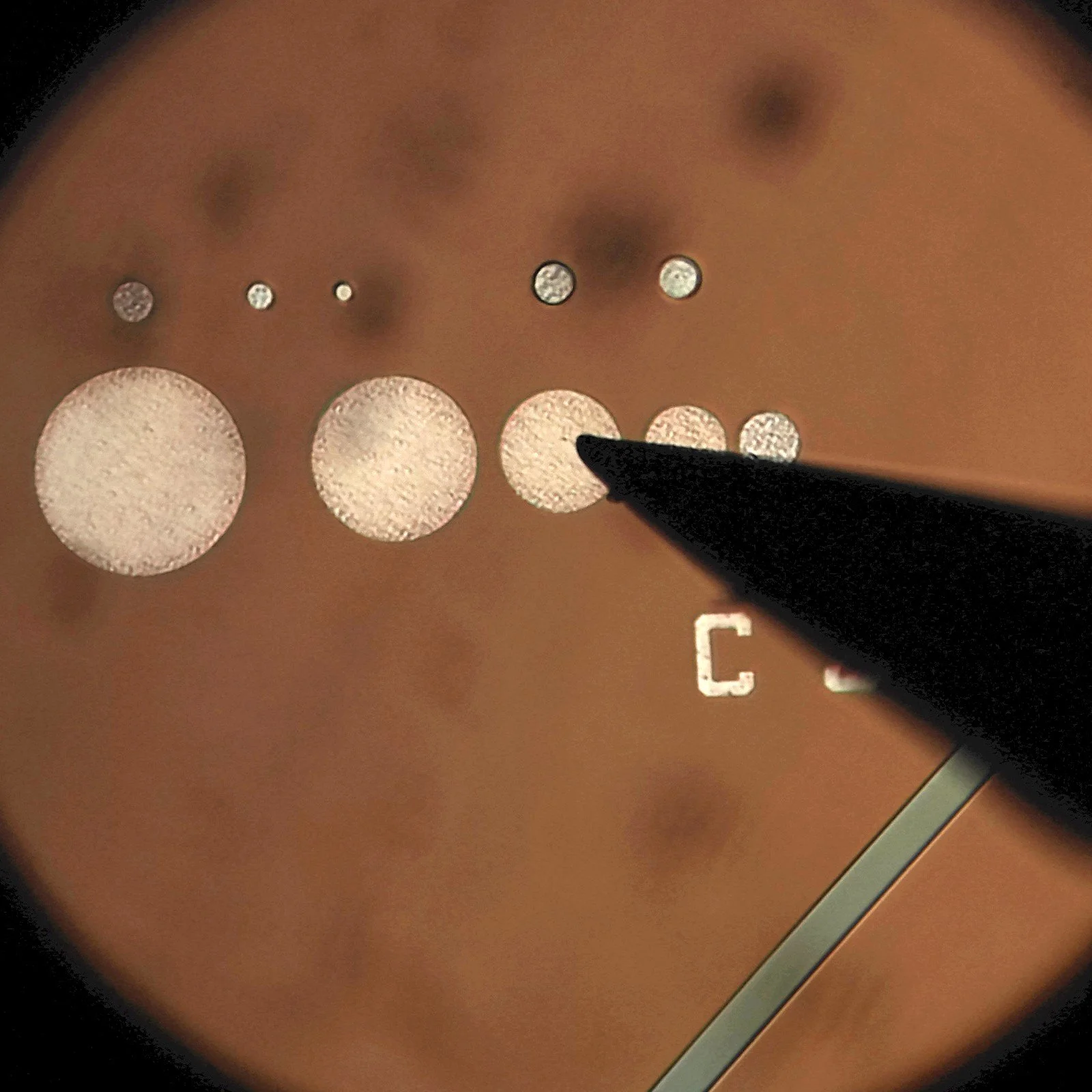 Close-up view of semiconductor test structure with probe needle contacting patterned circular test pads for electrical measurement