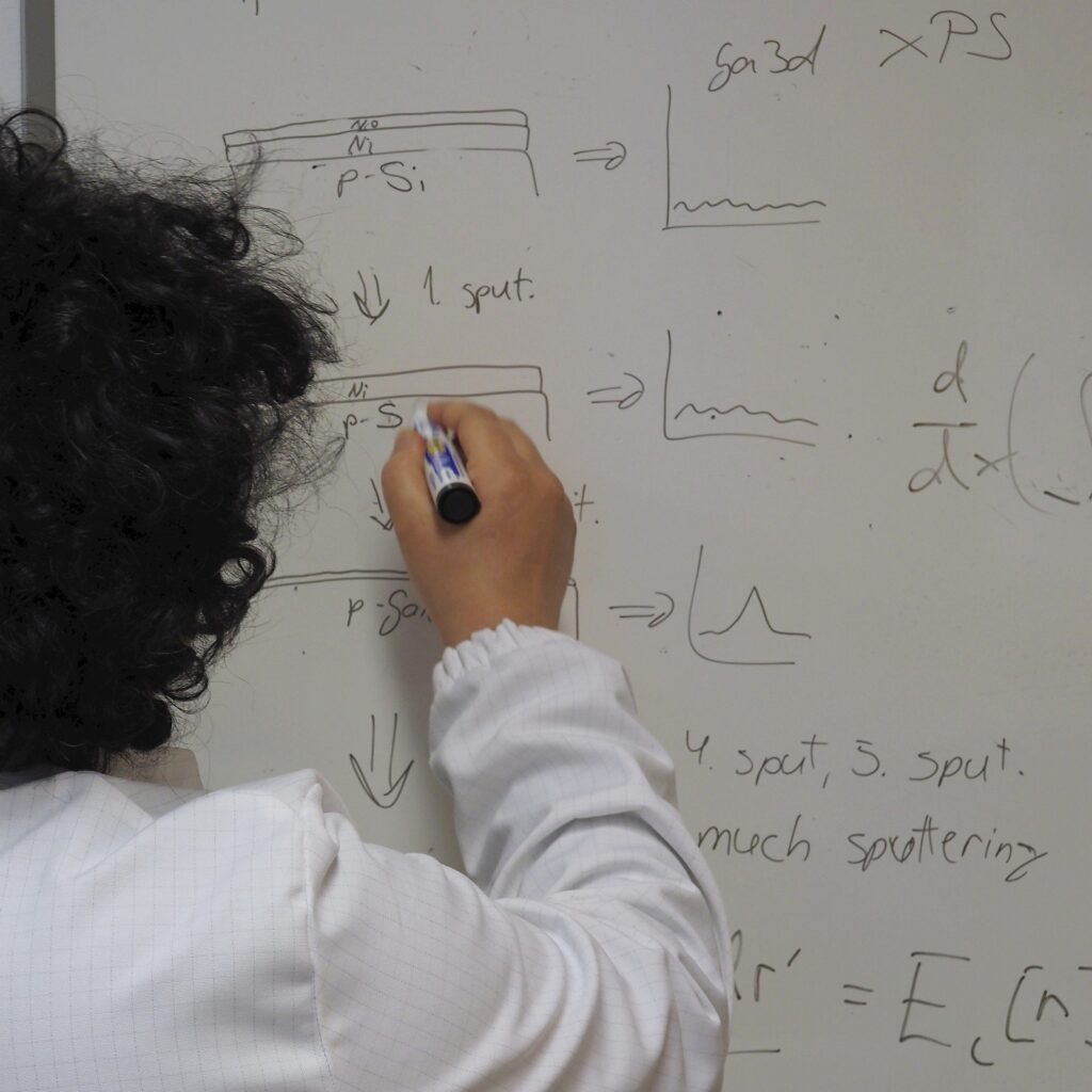 Scientist in cleanroom suit writing semiconductor process flow and data analysis graphs on whiteboard